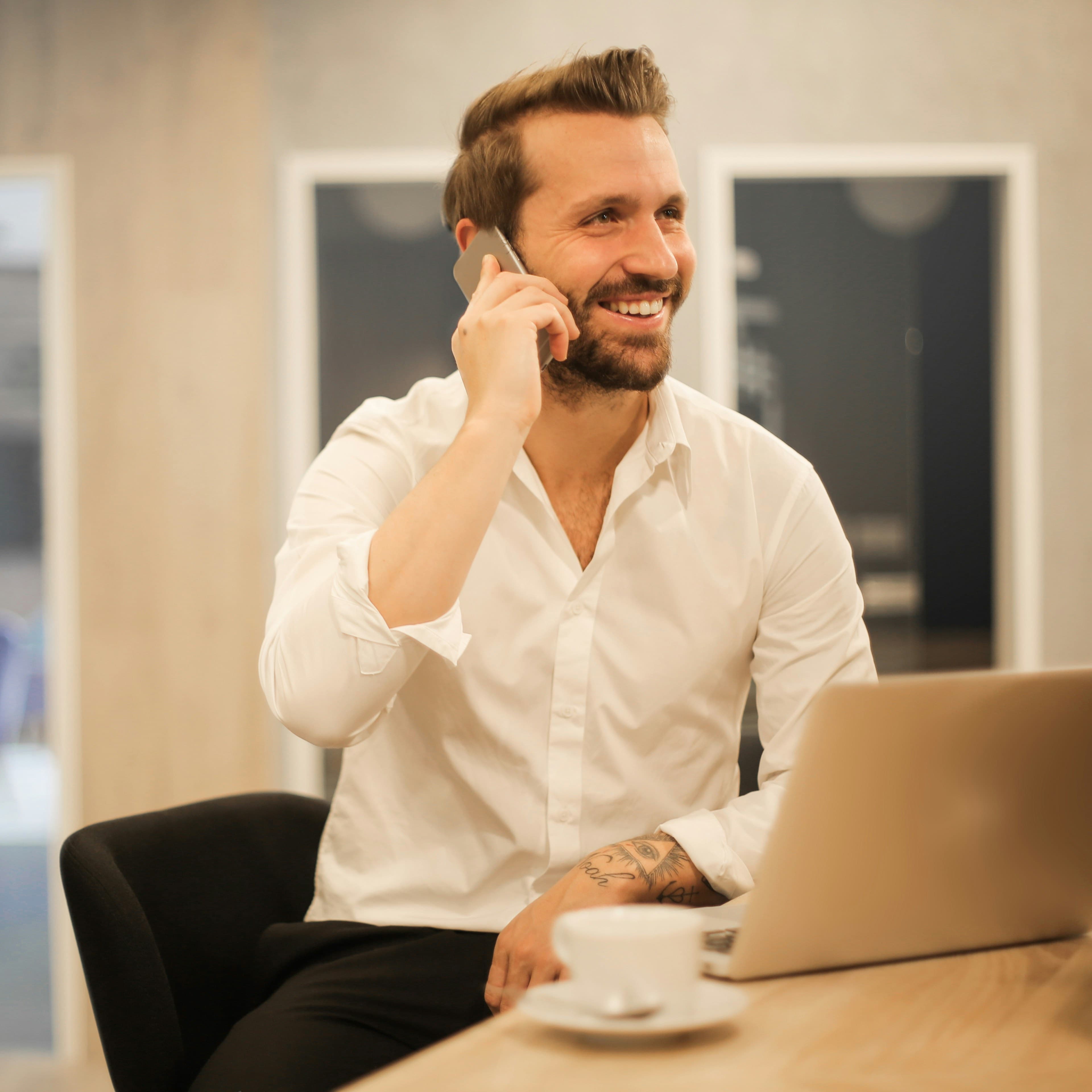 Un imprenditore al telefono, seduto con il portatile aperto davanti